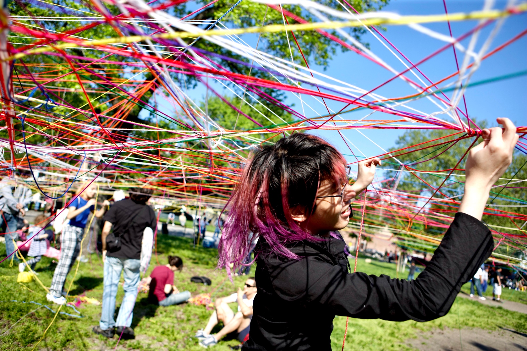 A visitor with magenta-streaked hair reaching up into an overhead web of multicolored strings